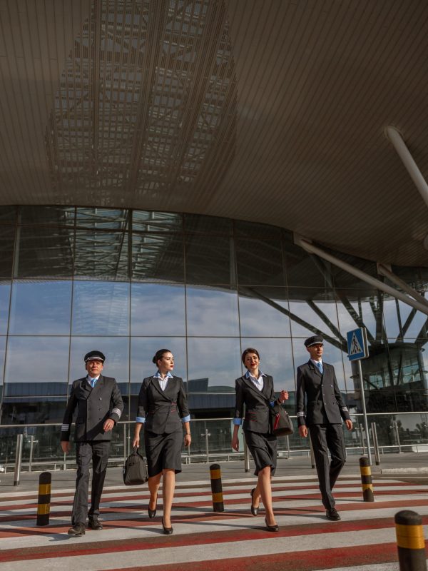 Full-length photo of two flight attendants with bags walking next to the pilots outdoor near airport terminal